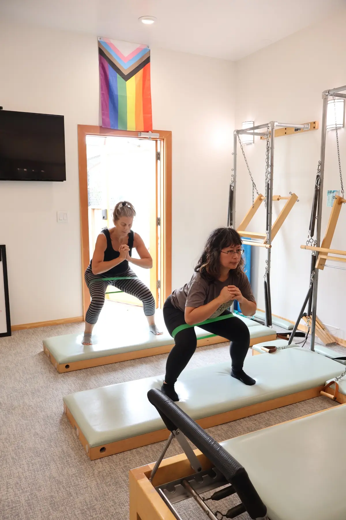 Two Pilates School students practicing supported squats with resistance bands in the Geary studio