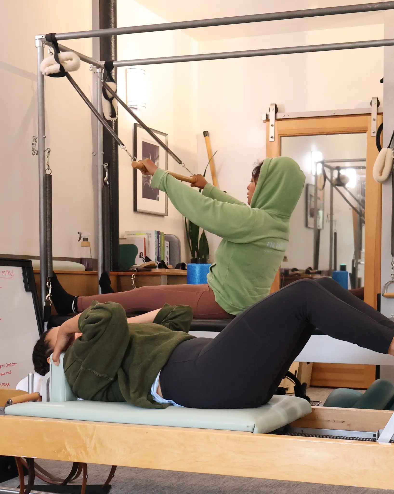 Two Pilates School students practicing on Classical Pilates equipment with their instructor